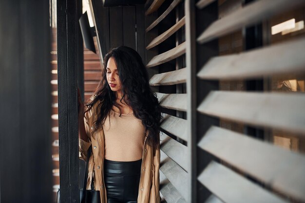 Woman with black curly hair standing near wooden windows