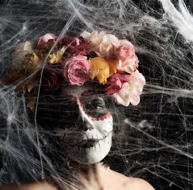 woman with black hair is dressed in a wreath of multi-colored roses and makeup is made on her face Sugar skull to the day of the Dead