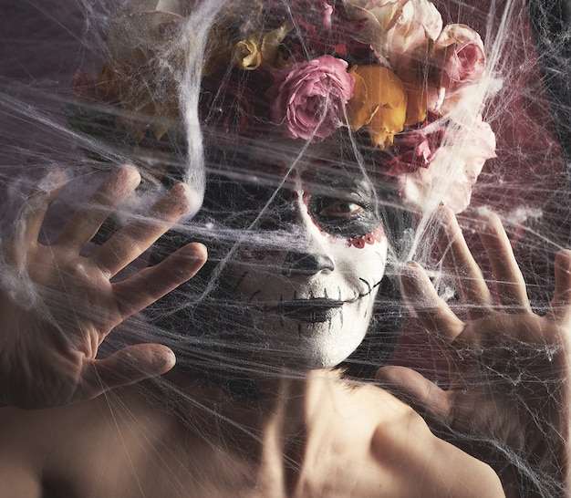 woman with black hair is dressed in a wreath of multi-colored roses and makeup is made on her face Sugar skull to the day of the Dead