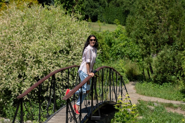 Woman with black hair and in jeans and a shirt and glasses in a summer park