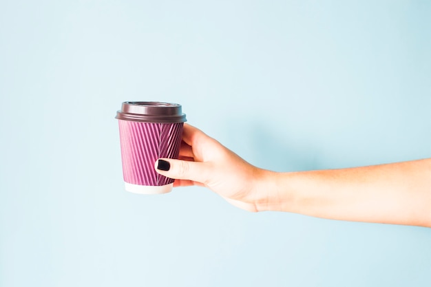 A woman with a black manicure holds in her hand a purple paper kraft disposable cup with coffee 