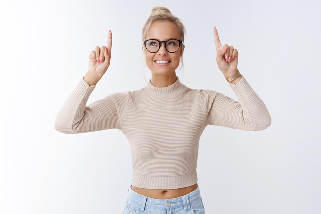 woman with blond hair in glasses looking prominent and bright pointing gazing up delighted with broad happy smile on white