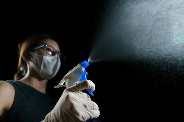 青い霧の消毒剤を噴霧してコロナウイルスまたはCOVID-19の拡散を止める女性。