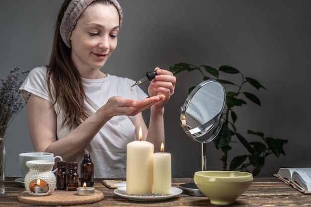 Woman with a bottle of natural oil for skin care Aroma lamp with essential oils candles on a table Concept of organic cosmetics aromatherapy morning and evening rituals relaxing atmosphere