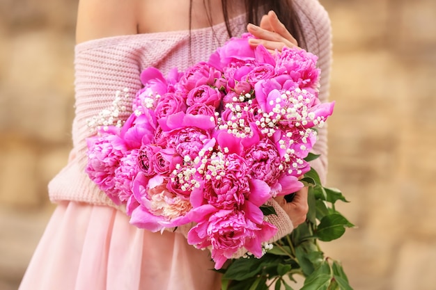 屋外で美しい牡丹の花の花束を持つ女性