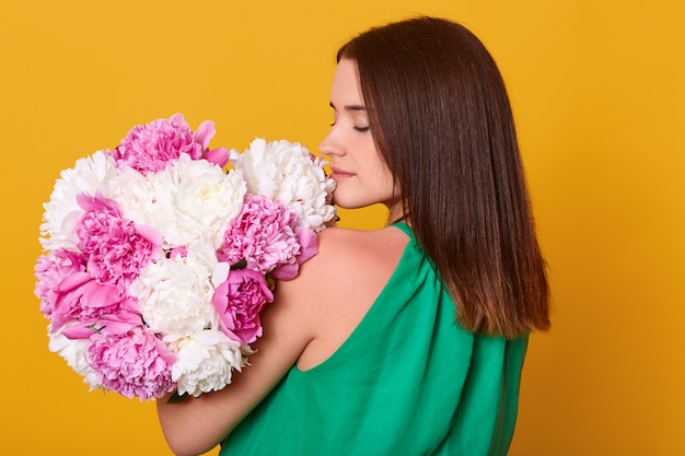 Donna con bouquet di peonie bianche e rosa nelle mani, in posa all'indietro, ragazza in abito trasparente chiaro