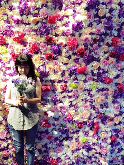 Foto donna con un bouquet in piedi contro un muro coperto di fiori