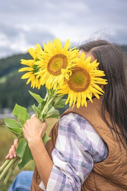 山岳地帯の自然の中でひまわりの花束を持つ女性