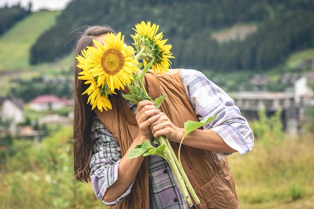 山岳地帯の自然の中でひまわりの花束を持つ女性