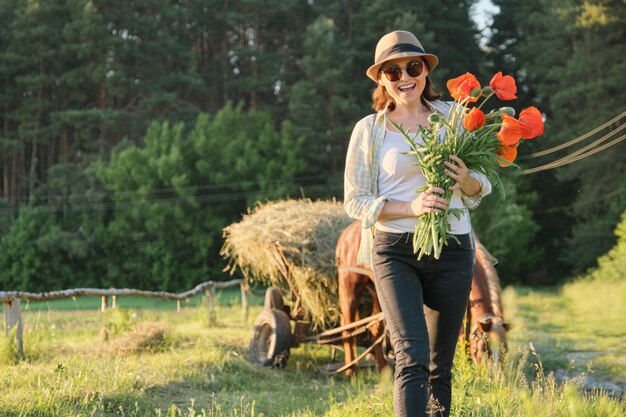 Donna con i mazzi di papaveri che camminano lungo la strada campestre