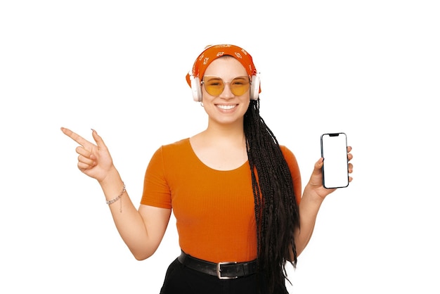 Woman with box braids is holding a phone while she is pointing away listening to music is wearing an orange shirt