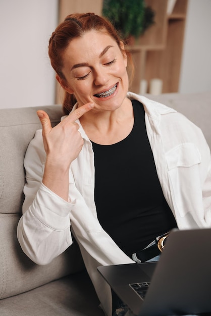 Woman with braces having consultation with orthodontist on video call and pointing finger at braces