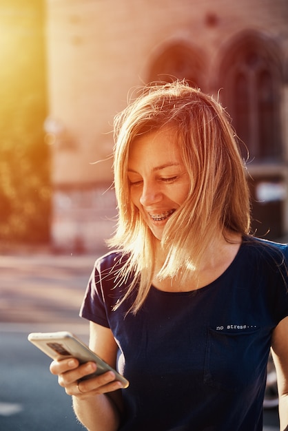 Foto donna con bretelle che utilizza smartphone in una strada della città