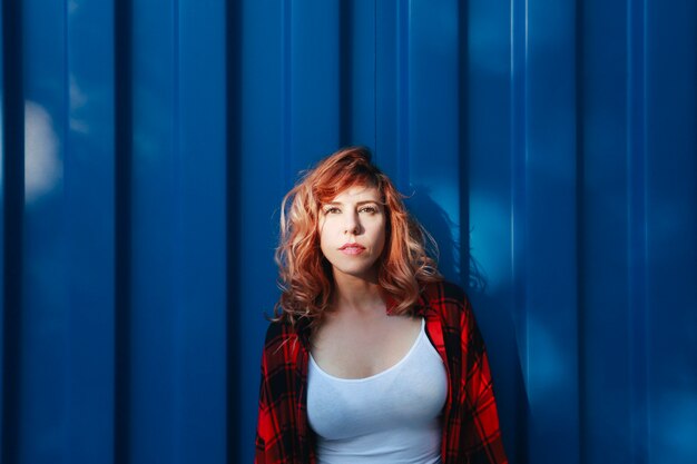 Woman with bright eyes and plaid shirt leaning on a blue container outdoors