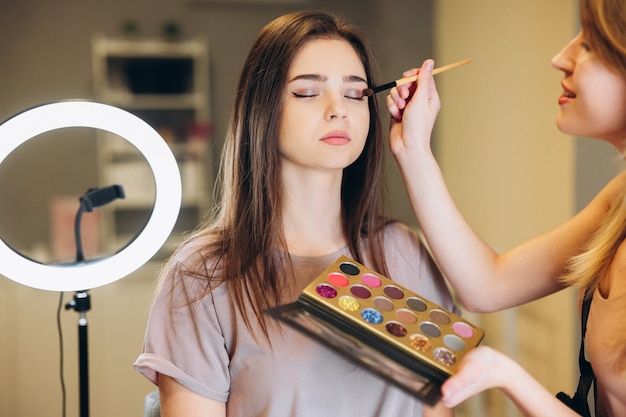 Photo woman with brown hair and closed eyes does makeup. the makeup artist applies glittering shadows to the eyelids.