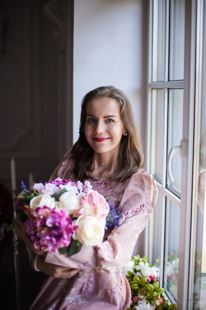 Woman with brown hair and red lips dressed in a pink dress