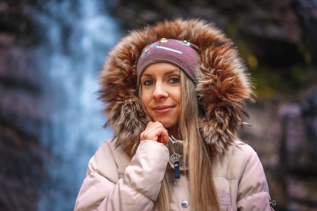 a woman with brown jacket and a hat near a waterfall