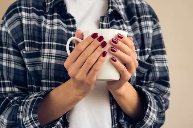 Woman with a burgundy manicure in plaid shirt holding white cup