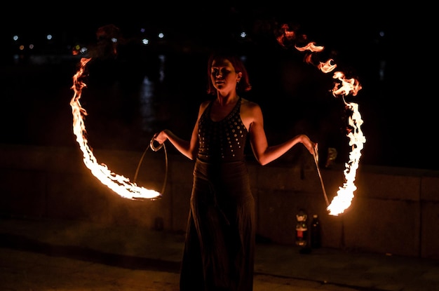 A woman with burning torches on the street at night.