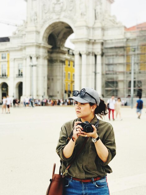 Photo woman with camera looking away while standing against historic building