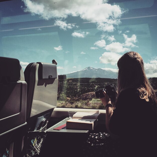 山を見ながら電車に座っているカメラを持った女性