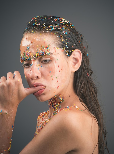 Женщина с конфетами посыпает губы, держа большой палец во рту