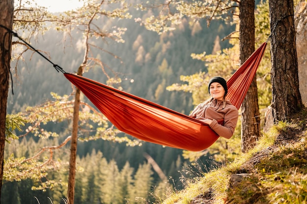 Woman with cap resting in comfortable hammock during sunset Relaxing on orange hammock between two trees pine enjoying the view