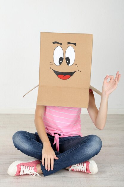 Photo woman with cardboard box on her head with happy face near wall