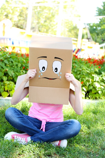 Photo woman with cardboard box on her head with sad face, outdoors