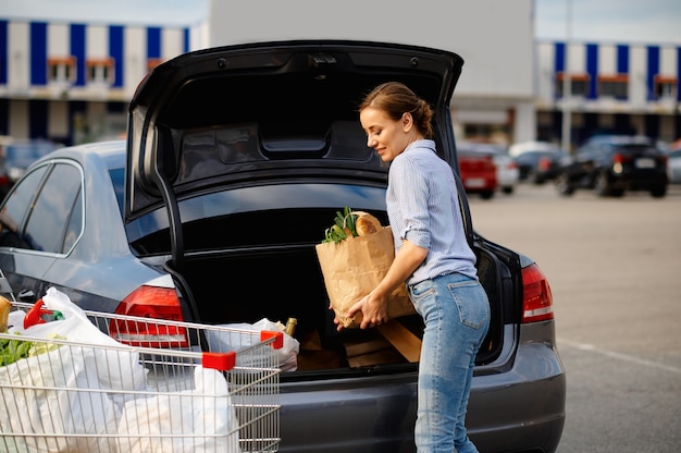 La donna con il carrello mette i suoi acquisti nel bagagliaio dell'auto