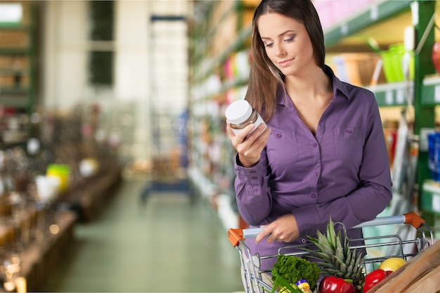 Woman with cart shopping and holding buttle in supermarket