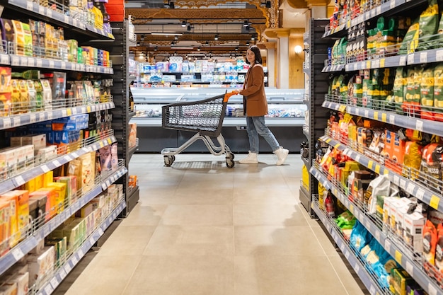 カートを持った女性が食料品店の棚の列の間を歩いている