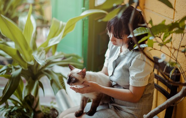 写真 椅子の上で植物のそばに座っている猫を持つ女性