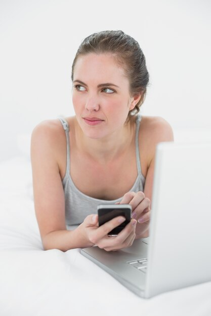 핸드폰과 노트북 침대에 누워있는 여자