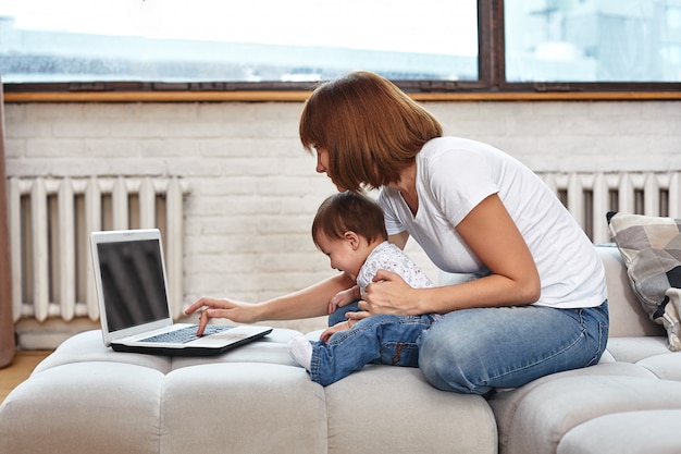 A woman with a child at a laptop sitting on a sofa. Work at home, freelancer, work during maternity leave for remote access.