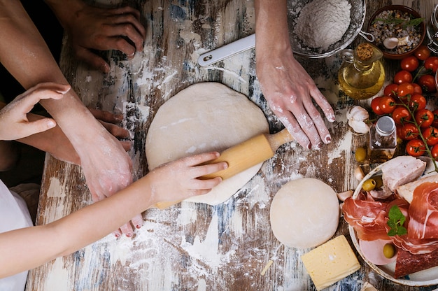 Woman with child preparing dough for homemade pizza. Light toning. Top view