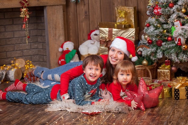 クリスマスツリーの横にあるサンタ帽子で肌の上に横たわる子供を持つ女性