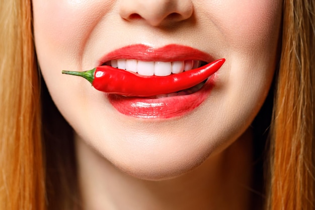 Woman with chili red pepper isolated en blue background sexy female lips hot seductive girl