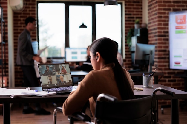 Woman with chronic impairment attending videocall meeting in\
disability friendly office, chatting with people on online\
videoconference. wheelchair user talking on remote\
teleconference.