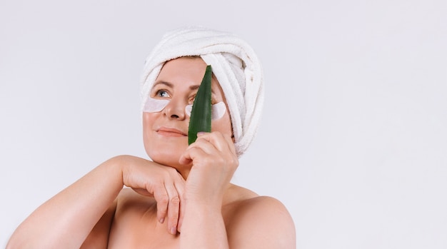 Foto una donna con la pelle pulita e un asciugamano sulla testa con in mano una foglia di aloe vera. concetto di cura della pelle sana su sfondo bianco con spazio laterale. foto di alta qualità