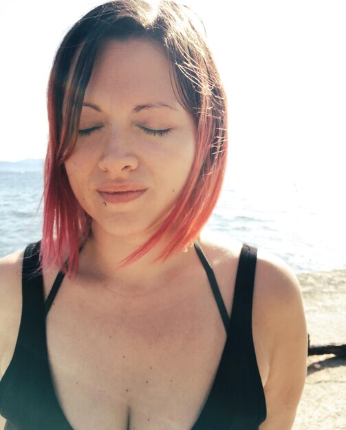 Photo woman with closed eyes against sea on sunny day