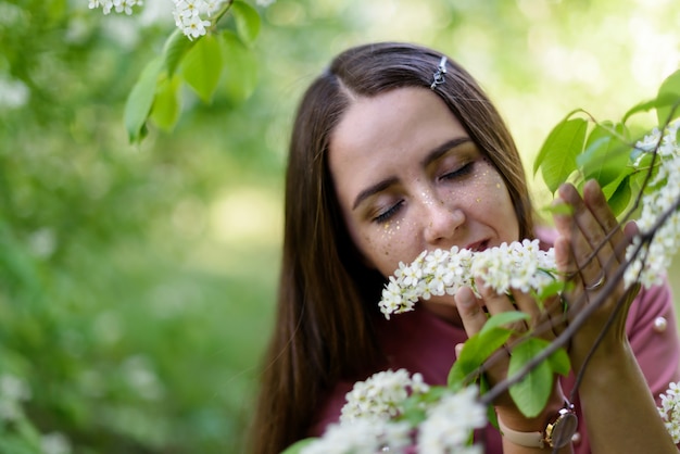 Woman with closed eyes sniffs flowers, relaxing and enjoying the sun in a blooming warm spring park