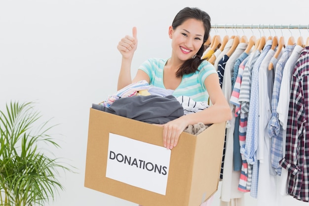 Donna con la donazione dei vestiti che gesturing i pollici su