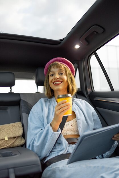 Woman with coffee and digital tablet on backseat of a car