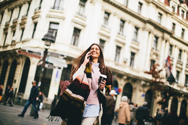 女性は行くためにコーヒーを持ち、手を携えて通りを歩いている女性