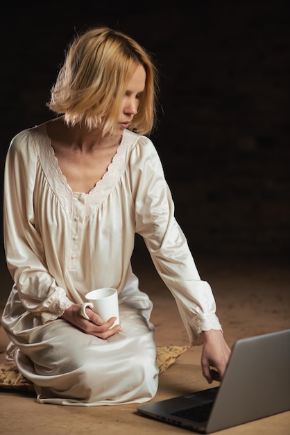 Woman with coffee and laptop Workaholism deadline concept Dark background Empty room