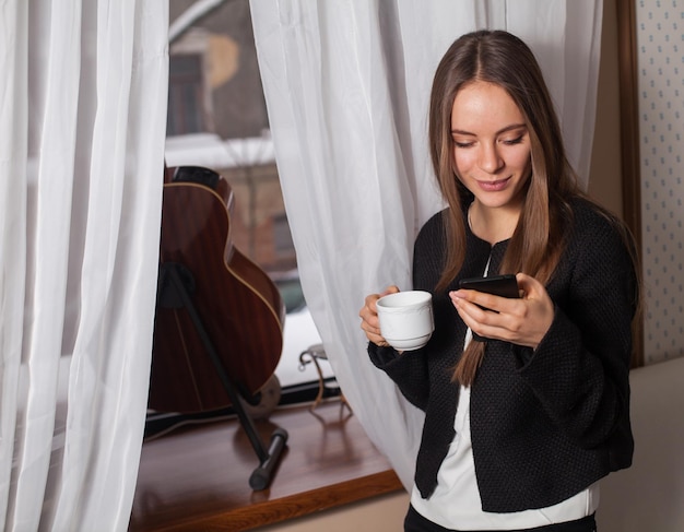 Woman with coffee standing behind guitar and drinking