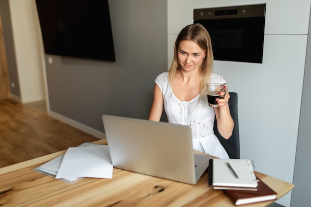 Donna con caffè che lavora al computer portatile in ufficio a casa