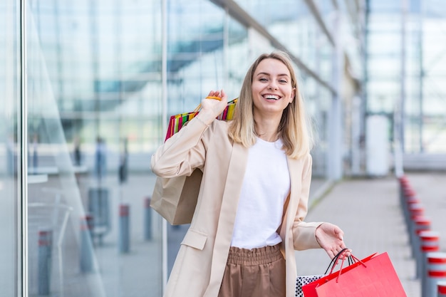 現代のショッピングモールの近くの商品と色のバッグを持つ女性