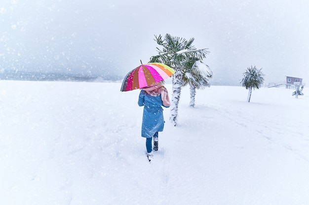 Woman with a colored umbrella among evergreen palm trees covered with snow